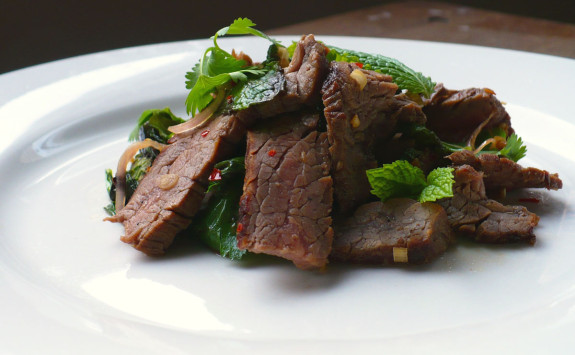 Grilled beef slices served on a bed of greens with fresh herbs.