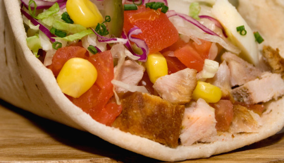 Close-up of a colorful pita sandwich with vegetables and meat.