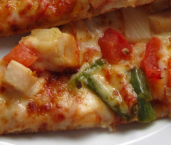 Close-up of a slice of pizza with chicken and vegetables.