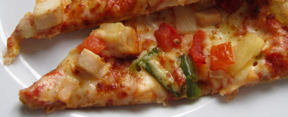 Close-up of a slice of pizza with chicken and vegetables.