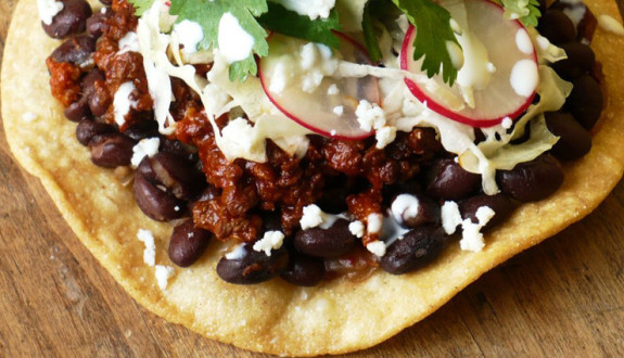 Close-up of a taco with ground meat, black beans, cheese, and radish slices.