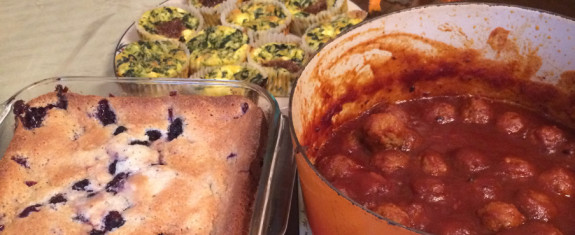 A blueberry cake and a jar of homemade apple sauce on a kitchen counter.