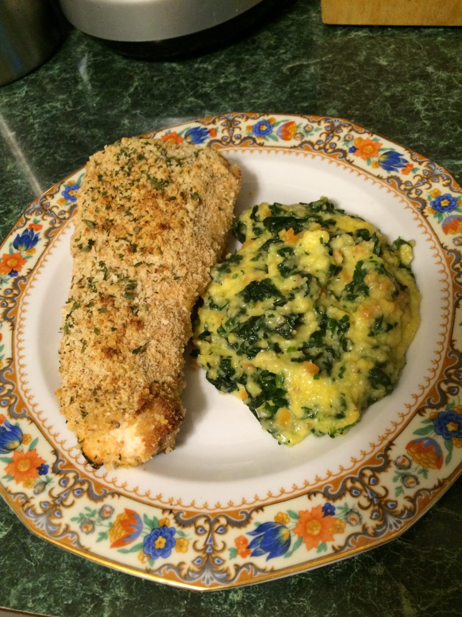 Herb-crusted chicken breast with creamy spinach polenta on a decorative plate.