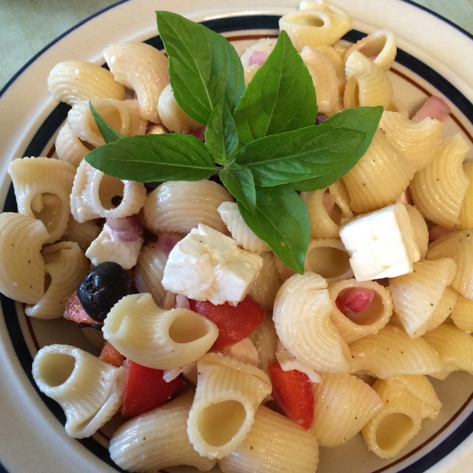 A fresh pasta salad with olives, feta, and basil garnish.