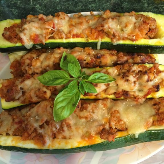 Three stuffed zucchini boats topped with melted cheese and fresh basil.