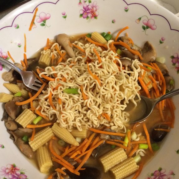 A bowl of ramen noodles with vegetables and two forks.