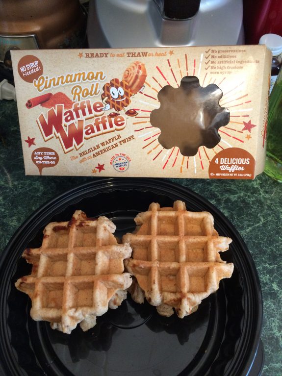 Two Belgian waffles on a black plate beside an empty waffle box.
