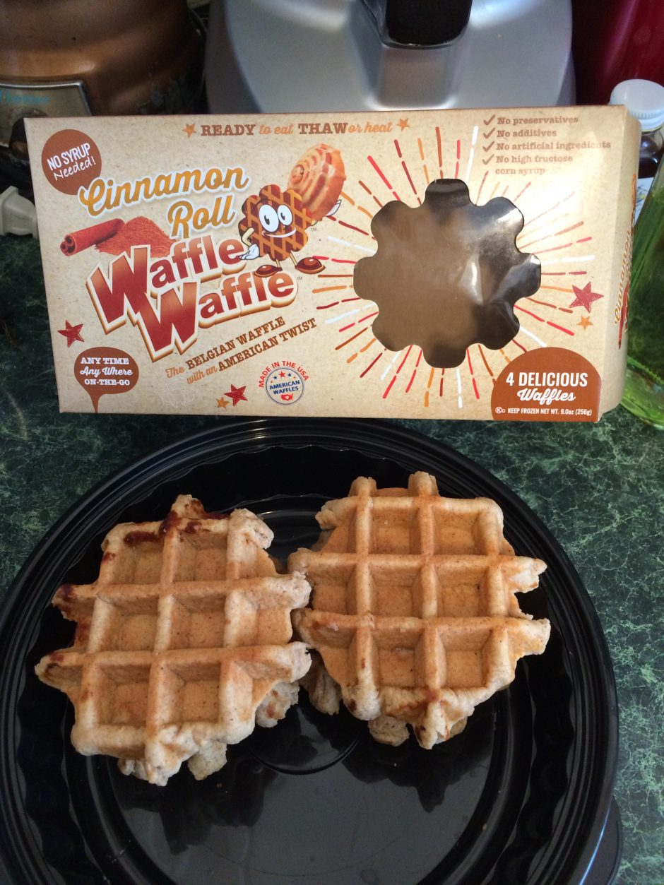Two Belgian waffles on a black plate beside an empty waffle box.