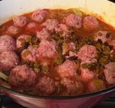 Meatballs cooking in tomato sauce with raisins.