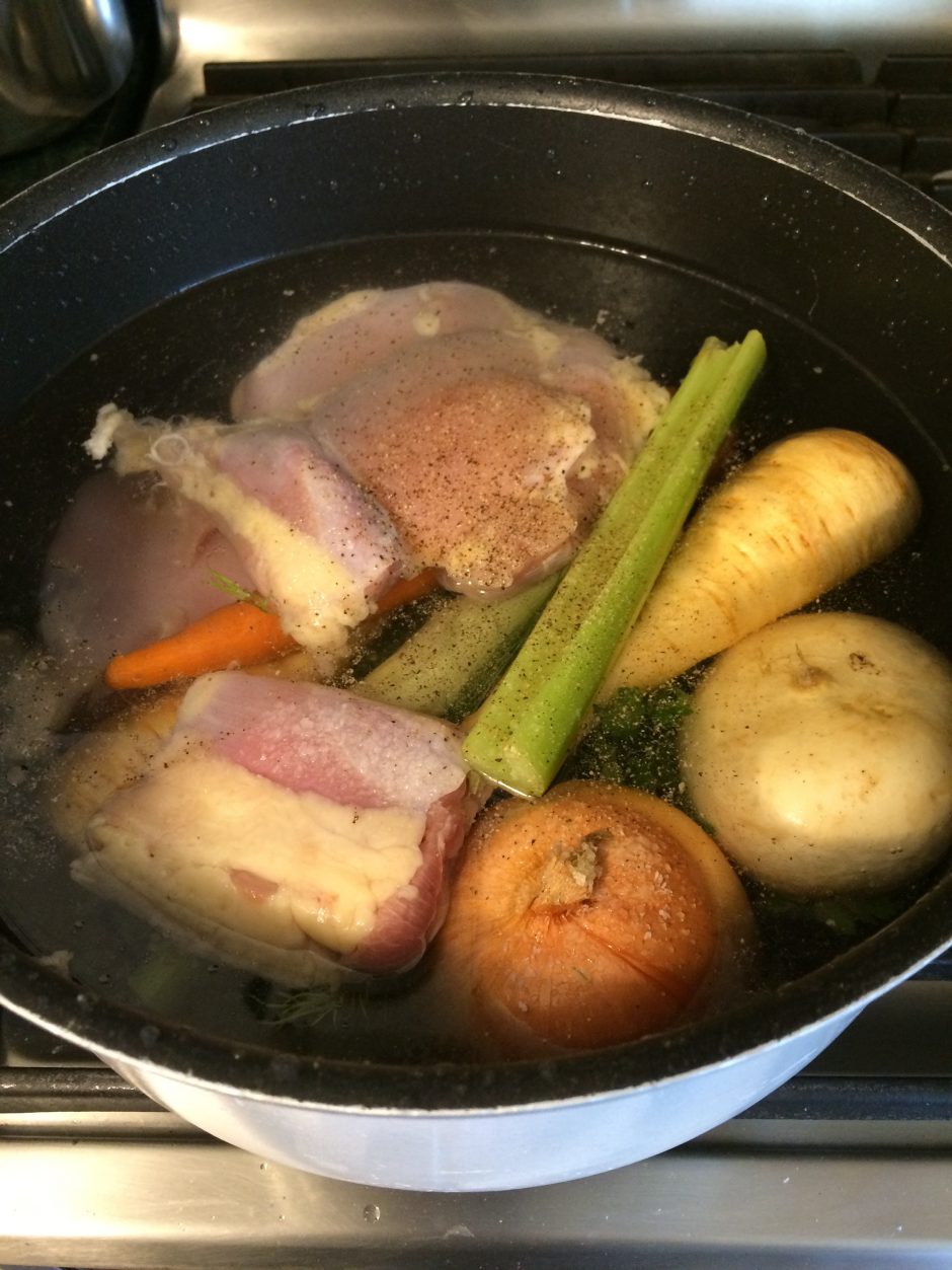 A pot with various vegetables and meat simmering in broth.