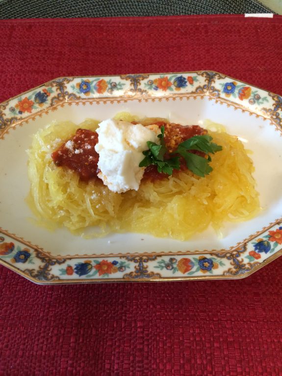 Spaghetti squash topped with tomato sauce and a dollop of ricotta cheese on a decorative plate.