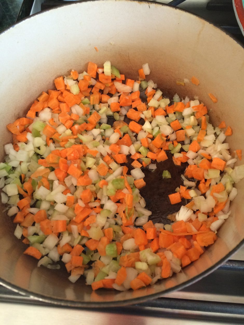Chopped onions, carrots, and celery cooking in a pot.