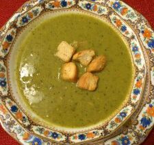 Green soup with croutons in ornate bowl.