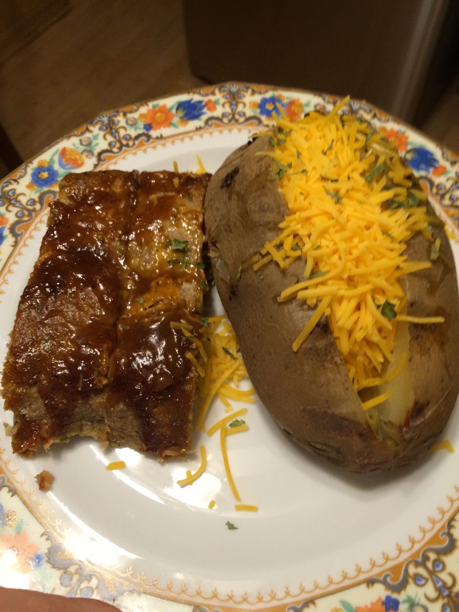 Barbecue ribs and a baked potato topped with shredded cheddar cheese on a decorative plate.