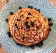 Pancakes topped with blueberries on blue plate.