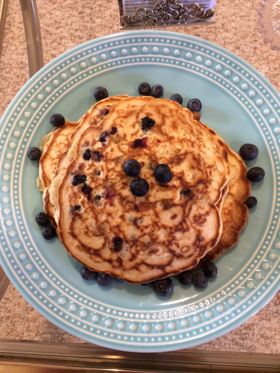 Stack of pancakes topped with blueberries on a patterned plate.