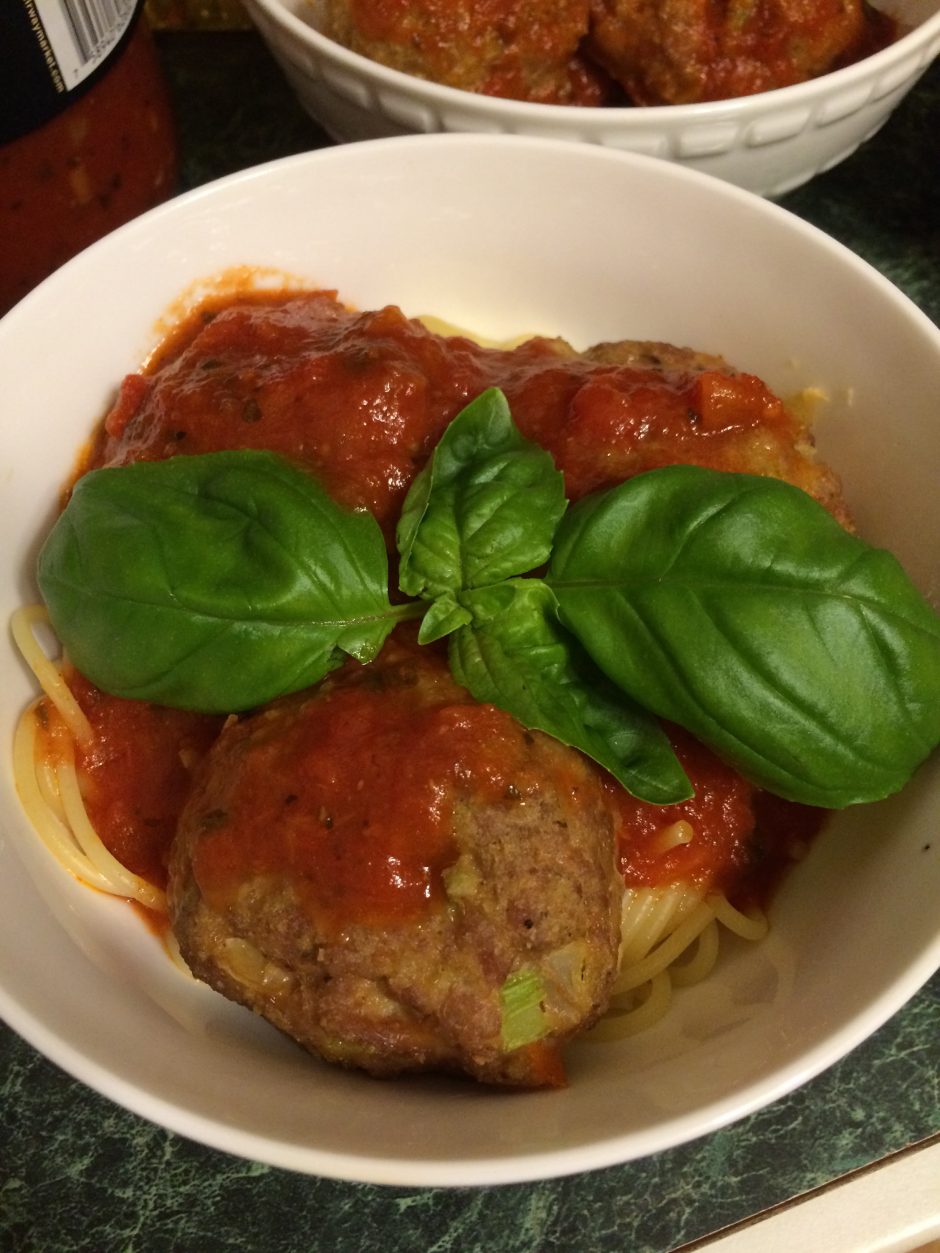 Bowl of spaghetti with meatballs, marinara sauce, and fresh basil.