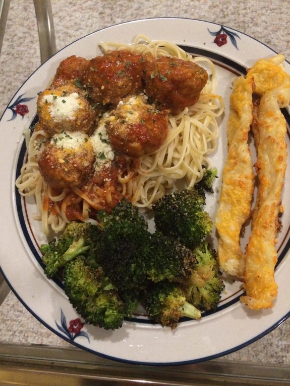 Plate with spaghetti, meatballs, broccoli, and breadsticks.