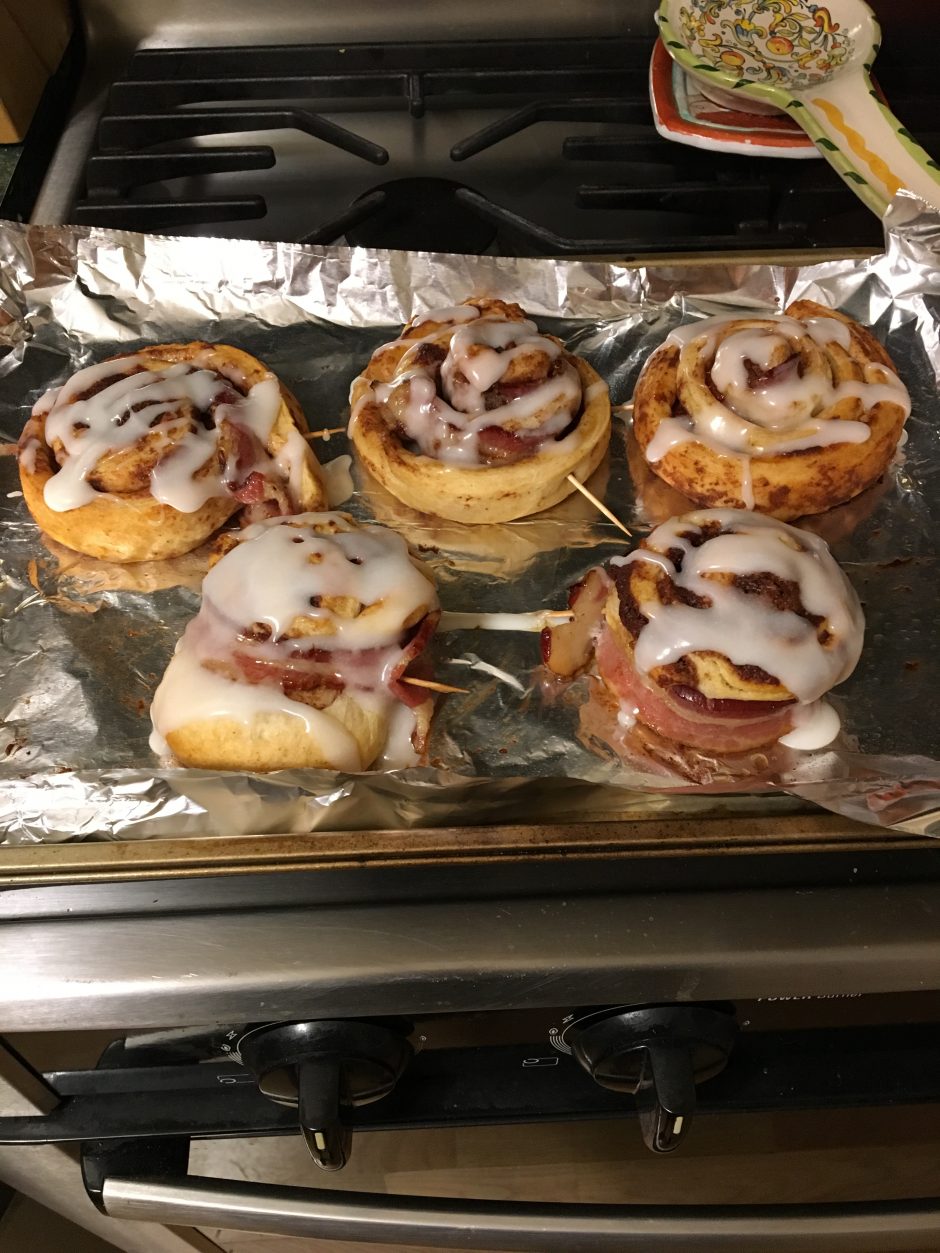 Freshly baked cinnamon rolls with icing on a foil-lined tray.