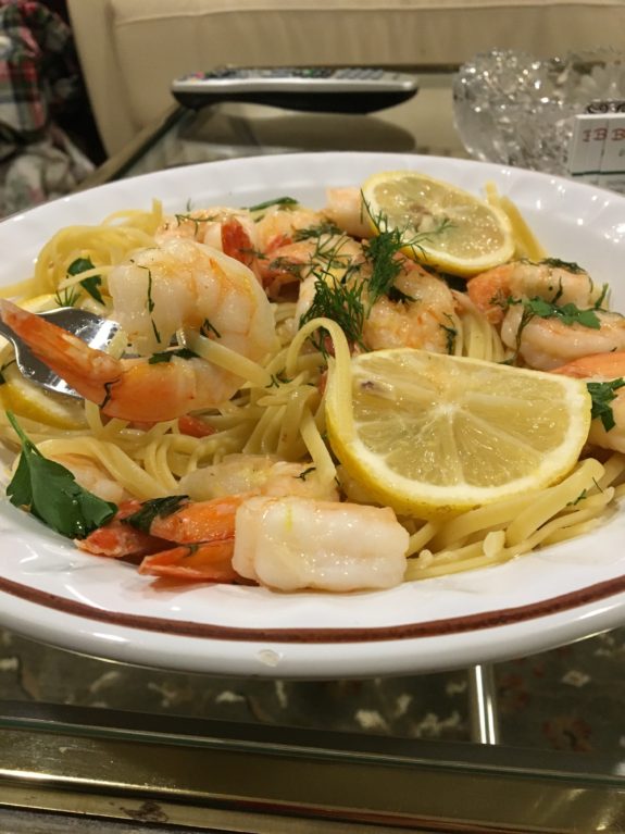 Plate of shrimp pasta garnished with lemon slices and herbs.