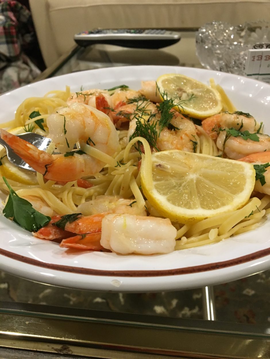 Plate of shrimp pasta garnished with lemon slices and herbs.