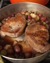 Pork chops cooking with vegetables in pan.