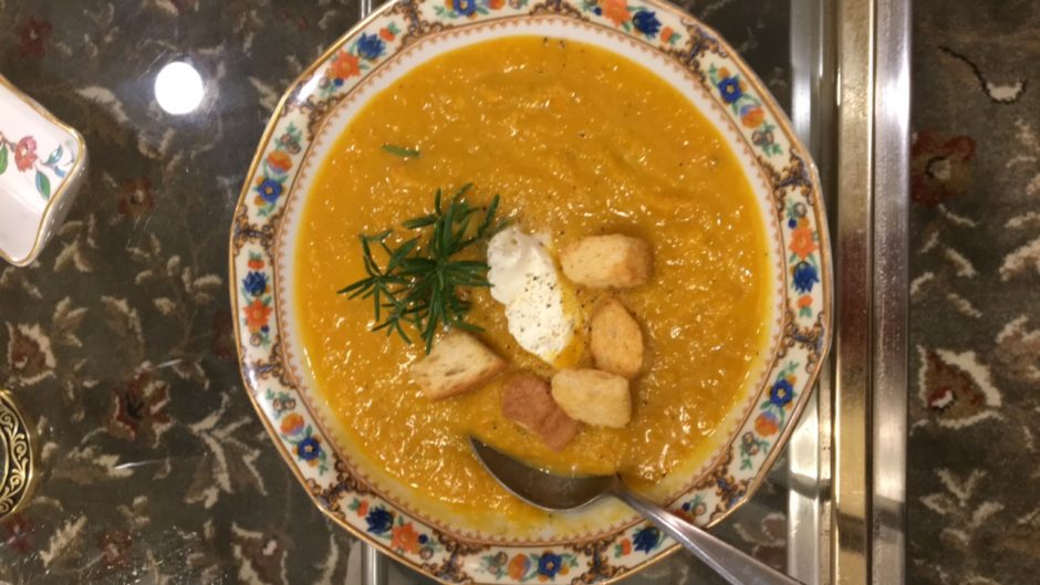 A bowl of creamy vegetable soup garnished with croutons, herbs, and sour cream.
