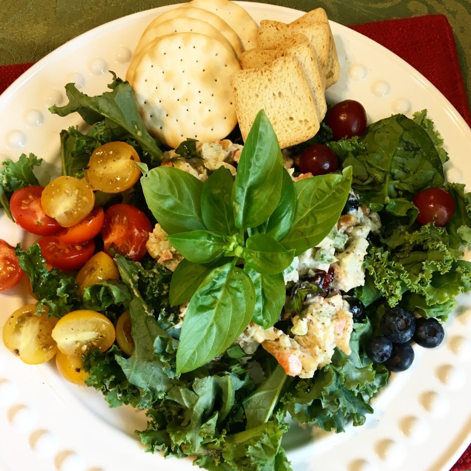 A fresh salad with kale, cherry tomatoes, blueberries, and a basil garnish.