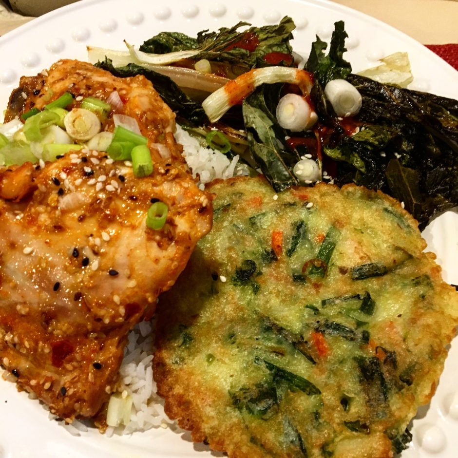 A plate with seasoned chicken, a vegetable pancake, and sautéed greens.