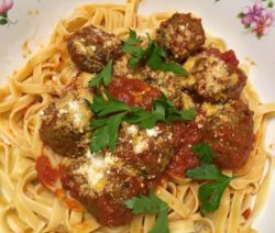 Plate of pasta with meatballs, tomato sauce, and parsley.
