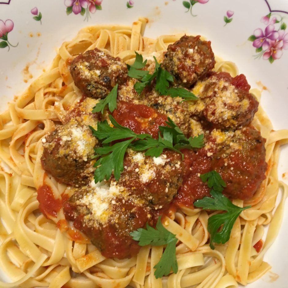 Plate of pasta with meatballs, tomato sauce, and parsley.