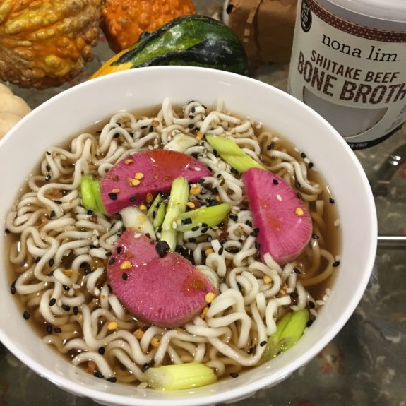 Bowl of ramen with slices of pink meat and green garnish.