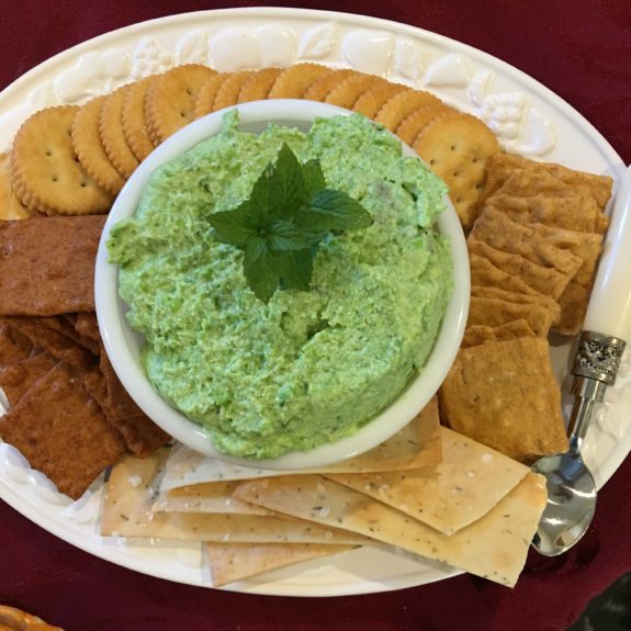 A plate with green dip and assorted crackers and pita bread.
