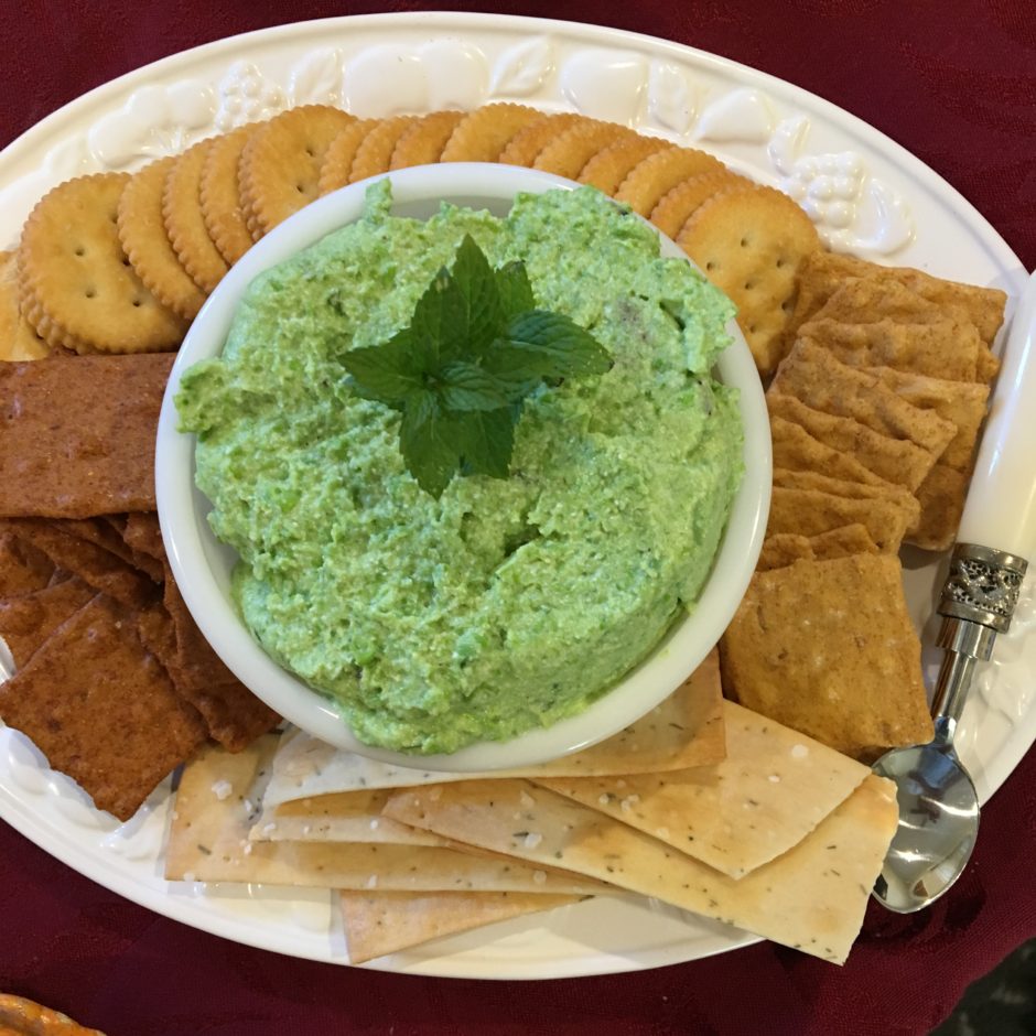A plate with green dip and assorted crackers and pita bread.