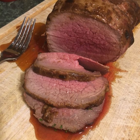 Juicy medium-rare roast beef sliced on a wooden cutting board.