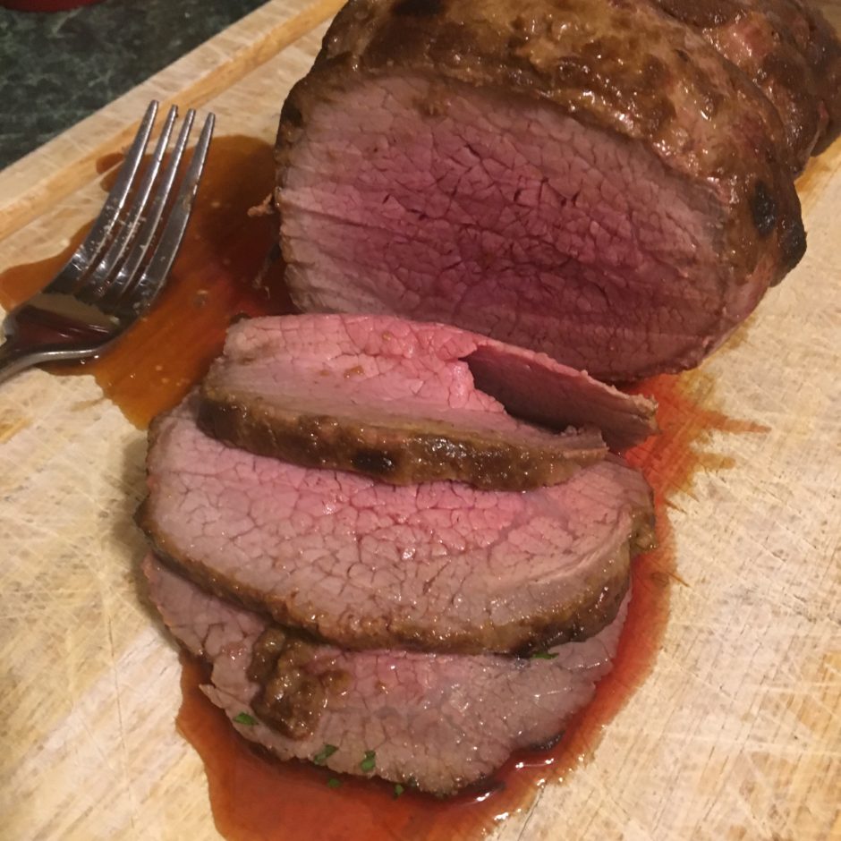 Juicy medium-rare roast beef sliced on a wooden cutting board.