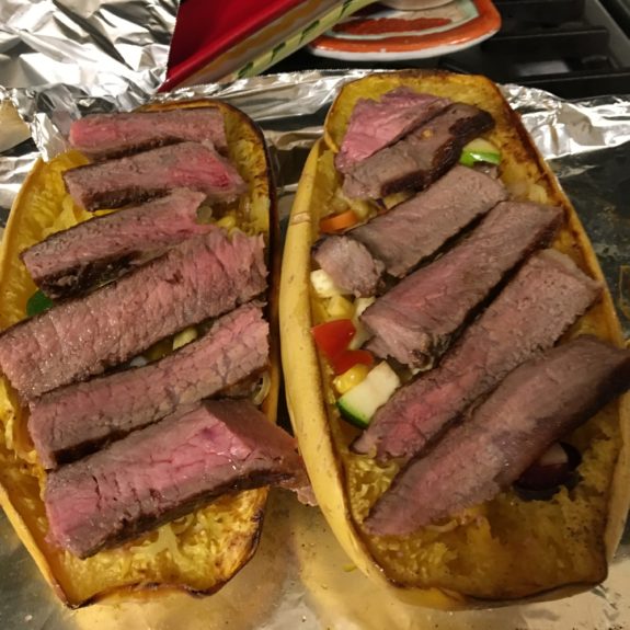 Two open-faced sandwiches topped with sliced steak and vegetables.