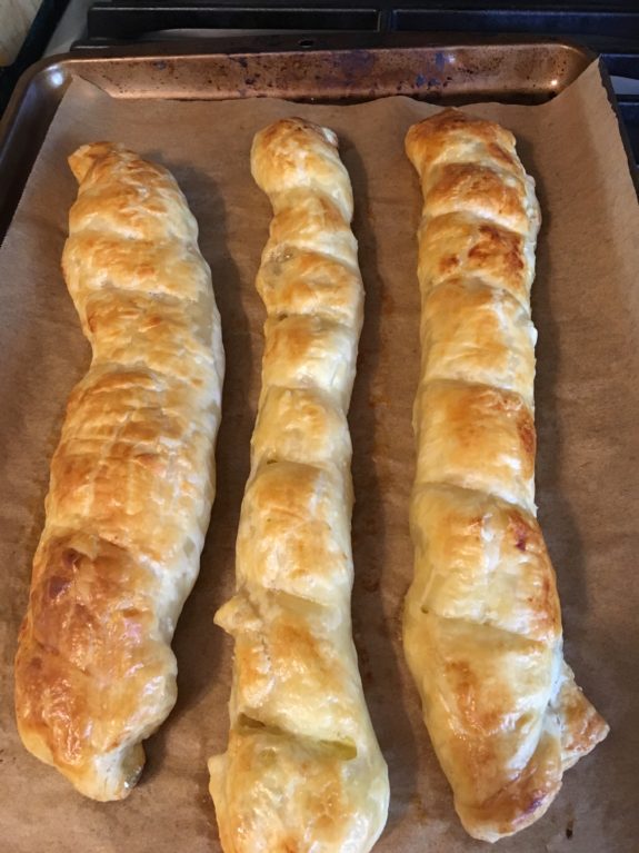 Four golden-brown braided breads on parchment paper.
