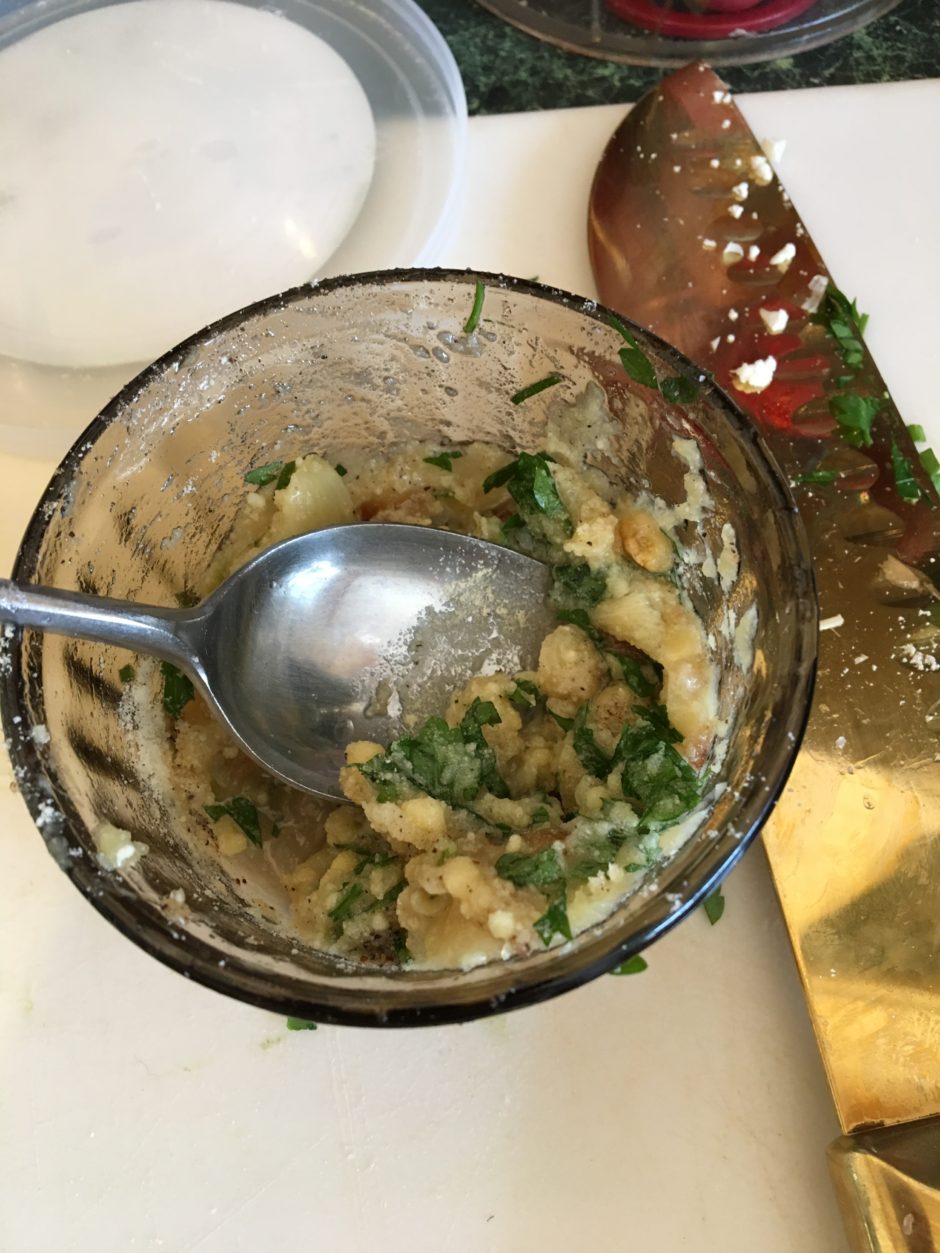 A nearly empty glass jar with a spoon and remnants of a green herb mixture.