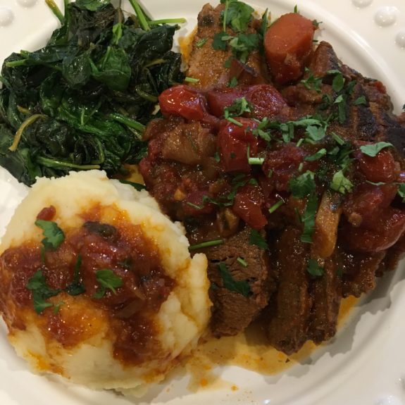 A plate with mashed potatoes, cooked greens, and a stew with vegetables.