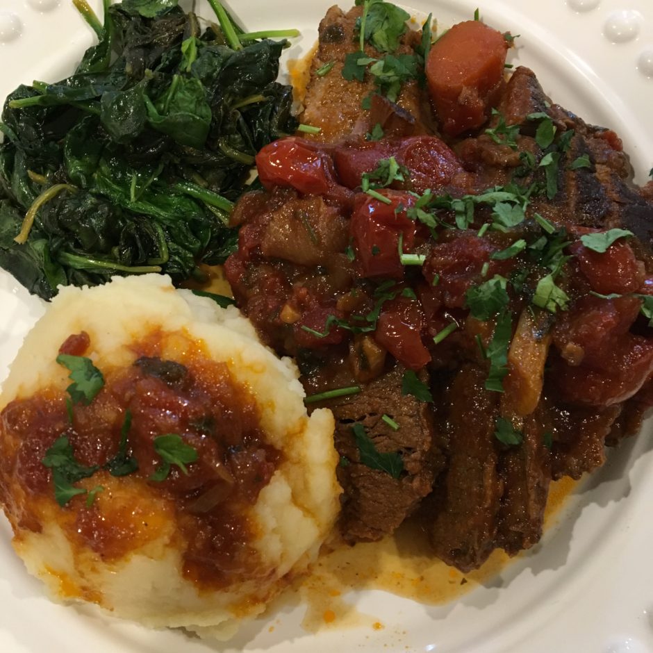 A plate with mashed potatoes, cooked greens, and a stew with vegetables.