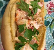 Lobster roll with parsley on floral plate.