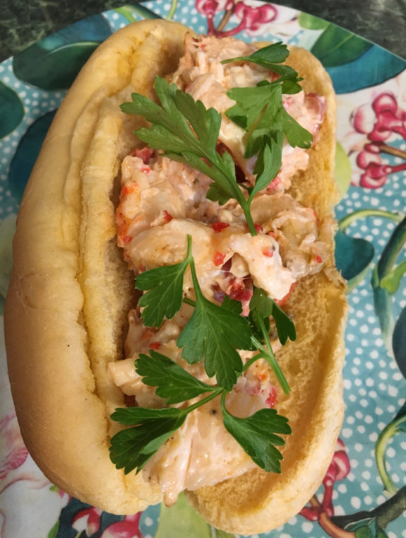 A lobster roll garnished with fresh parsley on a colorful tablecloth.
