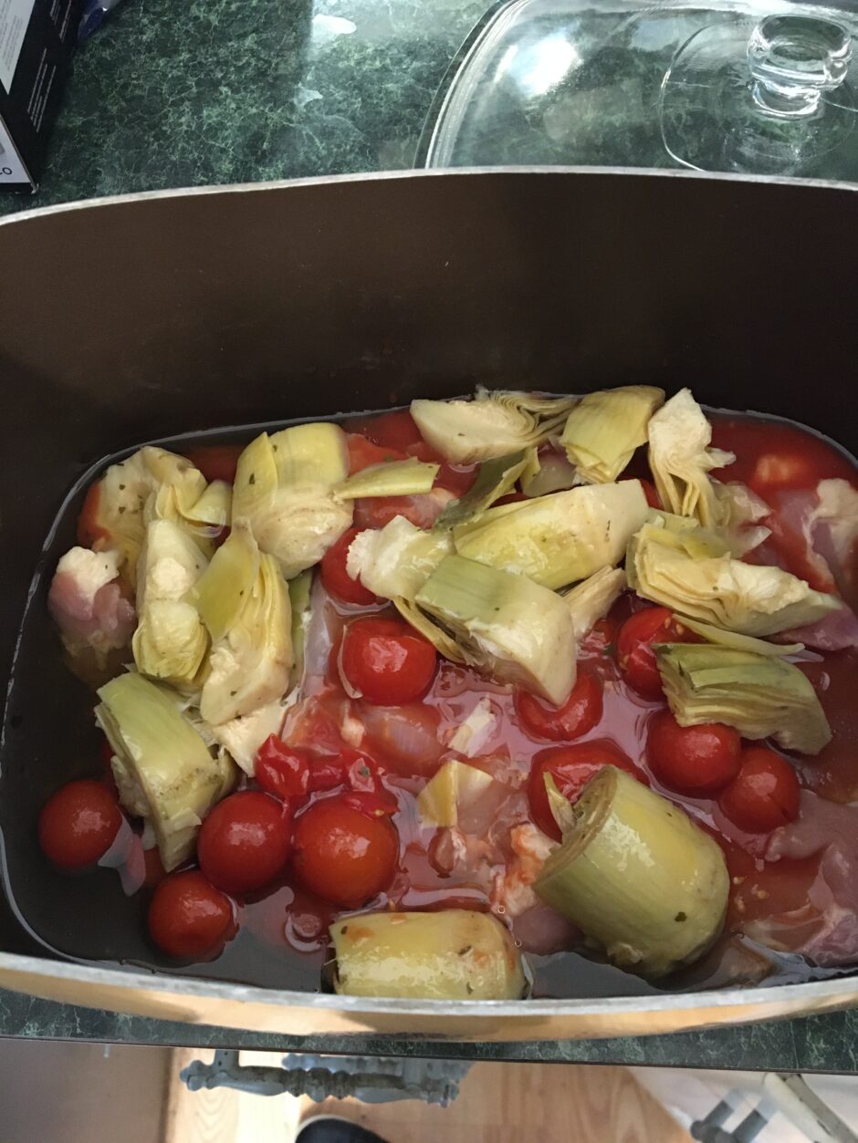 A pan of artichokes and cherry tomatoes in liquid.