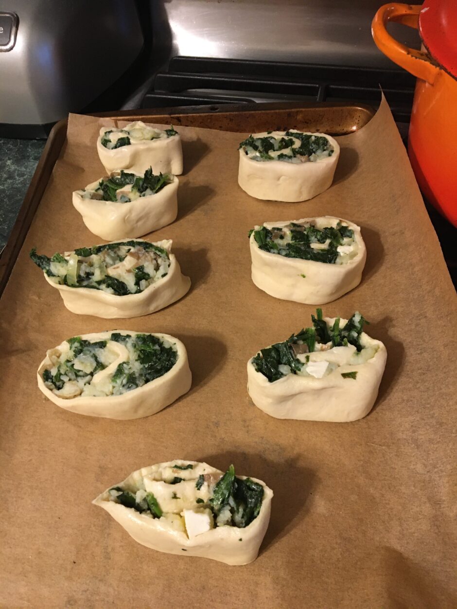 Unbaked spinach and cheese stuffed crescent rolls on parchment paper.