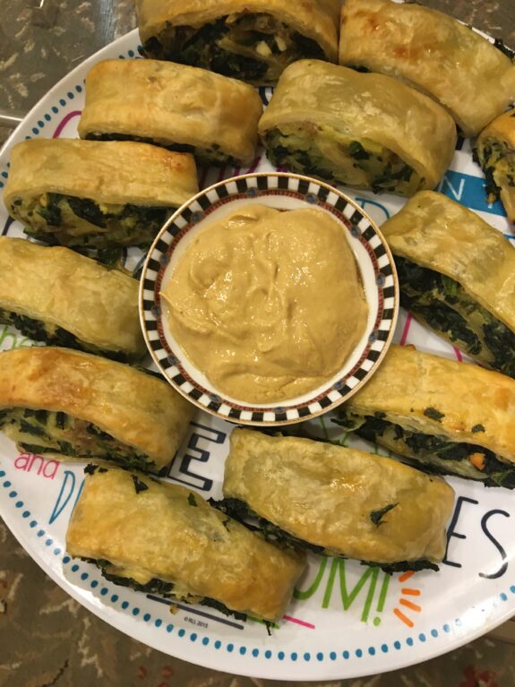 Golden brown spinach pastries with a dipping sauce in the center.
