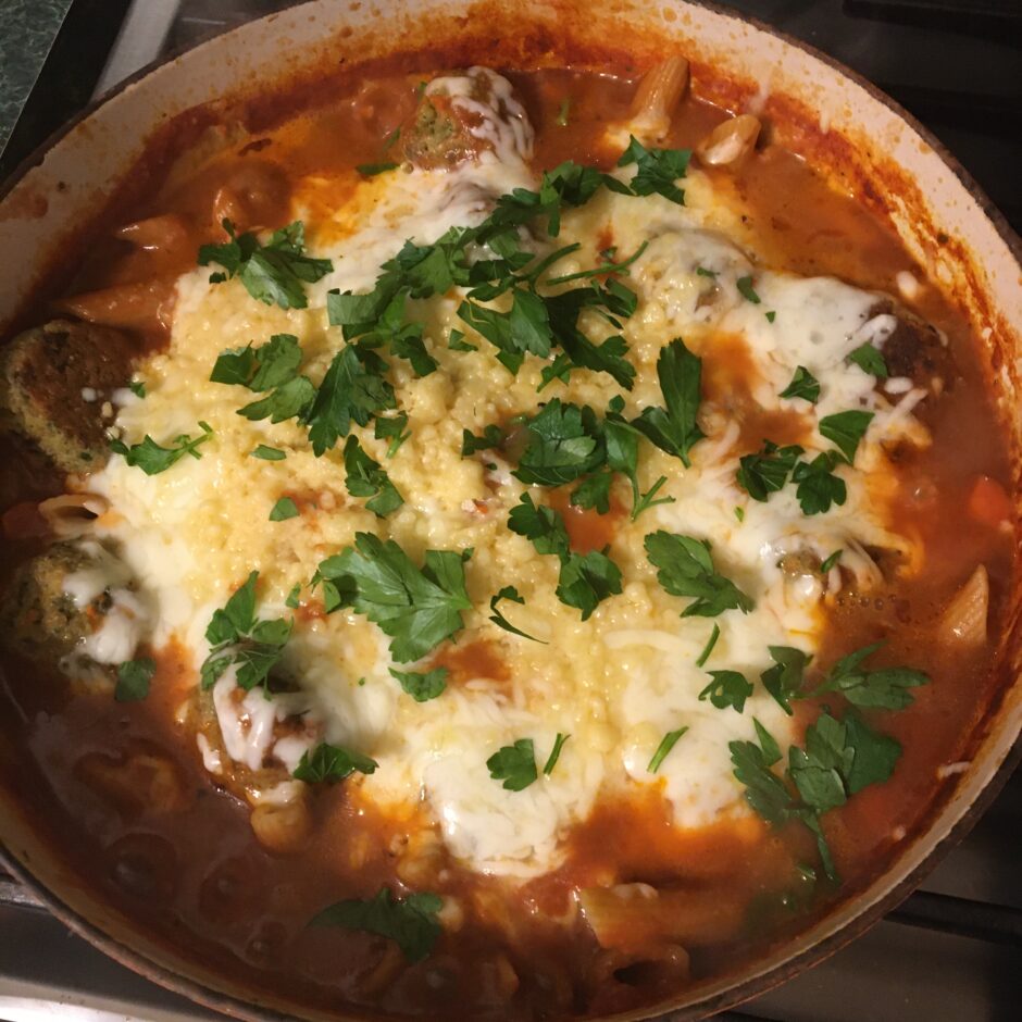 A cheesy baked dish topped with fresh herbs in a clay pot.
