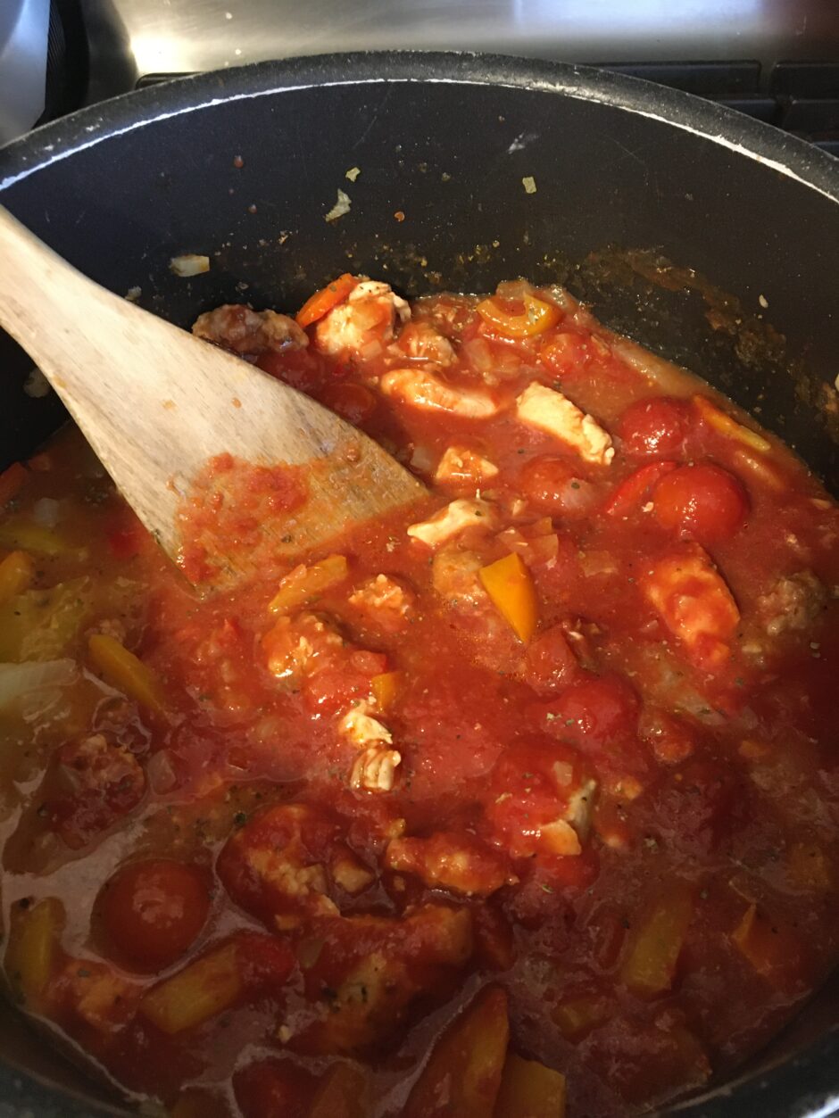 A pot of tomato sauce with chunks of chicken being stirred.