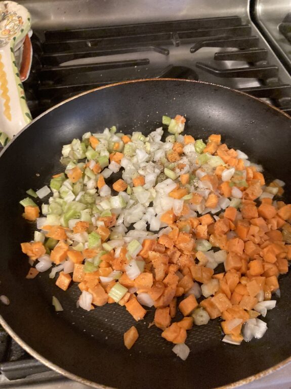Diced carrots, celery, and onions cooking in a pan.